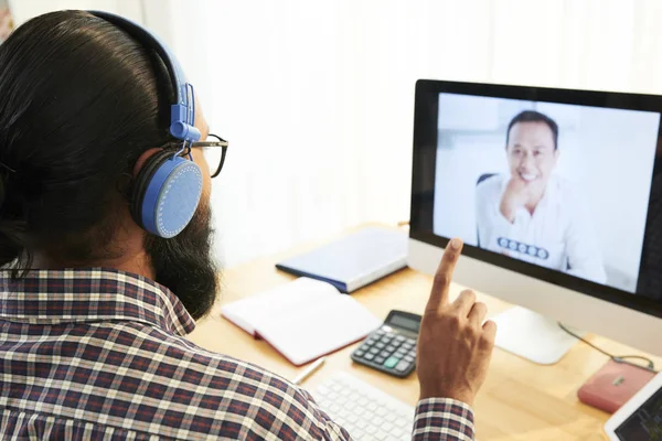 在耳机里通过视频聊天与同事在电脑屏幕上交谈的商人 — 图库照片