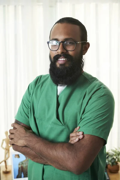 Bearded mix-raced medical specialist in uniform crossing his arms on chest while looking at you