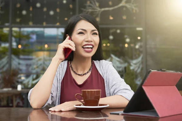 幸せなアジア女のテーブルにコーヒーとデジタル タブレットのカフェで座って 彼女の携帯電話で話しています — ストック写真