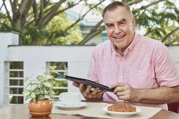 笑积极的老人吃早餐 在数字平板电脑上查看自己的社交媒体 — 图库照片