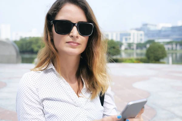 Young businesswoman in sunglasses managing her business via smartphone