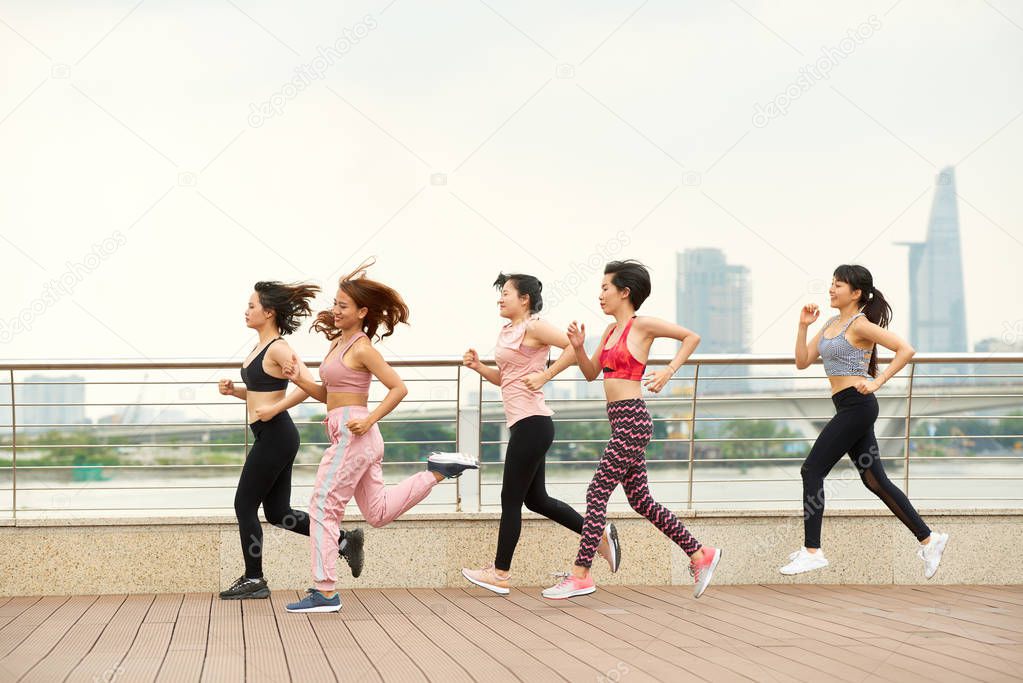 Side view of modern ethnic women in team jogging together on waterfront of city