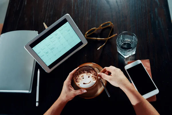 Businesswoman sitting at the table around wireless devices and enjoying a cup of delicious coffee