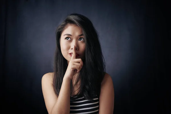 Portrait of Asian young woman asking to be quiet with finger on her lips isolated on black background