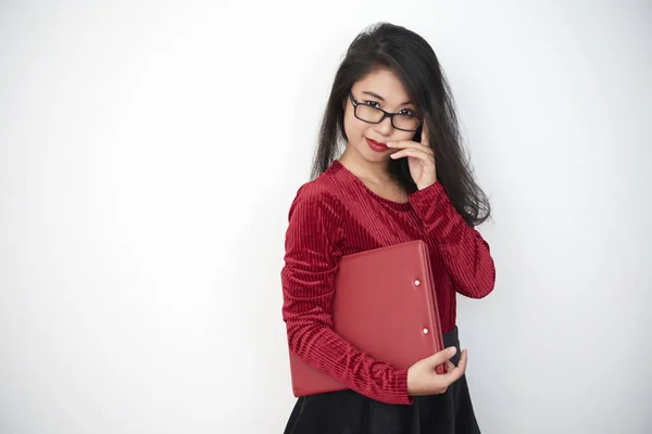 Portrait of serious Asian businesswoman in eyeglasses holding red folder and looking at camera