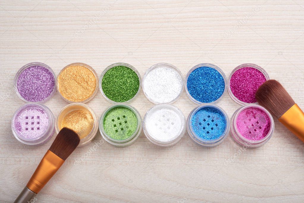 Top view of cosmetic glowing multicolored glitters in tiny cans composed in row with brushes