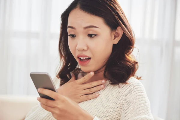 Pretty Vietnamese woman reading shocking news in smartphone