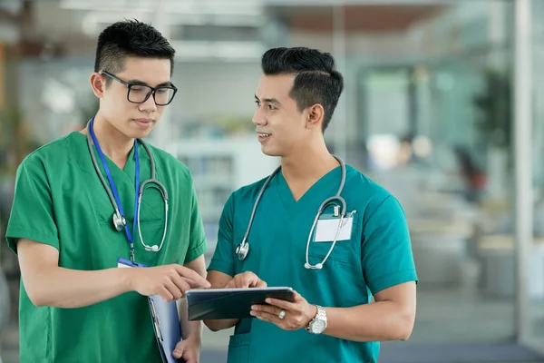 Két Fiatal Ázsiai Férfi Orvosi Scrubs Mutatva Információk Tablet Képernyőjén — Stock Fotó