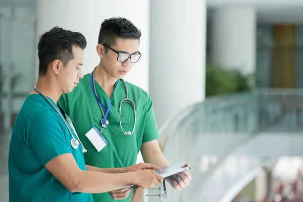 两名年轻的亚洲卫生专业人员站在医院的栏杆附近 在剪贴板上讨论病历的侧视图 — 图库照片