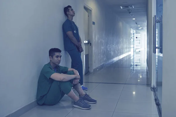 Sidovy Två Utmattade Asiatiska Män Scrubs Lutad Mot Väggen Korridoren — Stockfoto