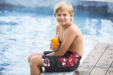 Yüzme havuzunun kenarında oturan ve taze portakal suyu içme boy gülümseyerek