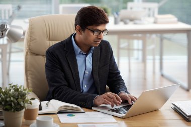 Ofiste dizüstü bilgisayar üzerinde çalışan bardaklarda Hintli işadamı 