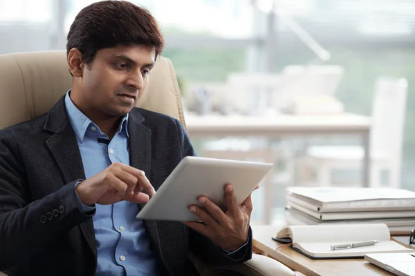 Portrait of Indian entrepreneur concentrated on work on digital tablet