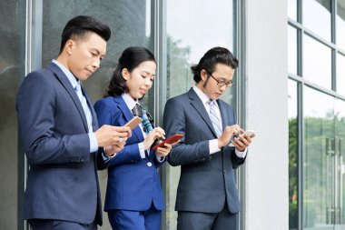 Grup genç Asyalı erkek ve kadın sörf akıllı telefonlar üzerinde sokak 