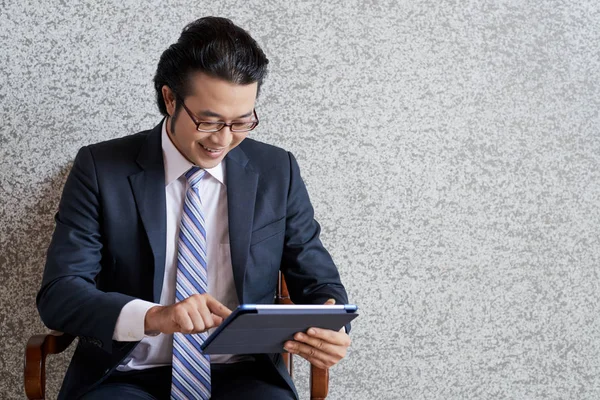 Jovem Asiático Terno Óculos Usando Tablet Enquanto Sentado Poltrona Parede — Fotografia de Stock