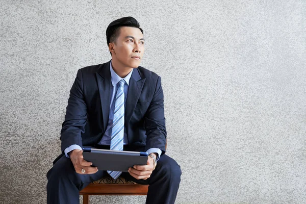 Adult Asian Man Sitting Tablet Armchair Looking Away Contemplation Gray — Stock Photo, Image