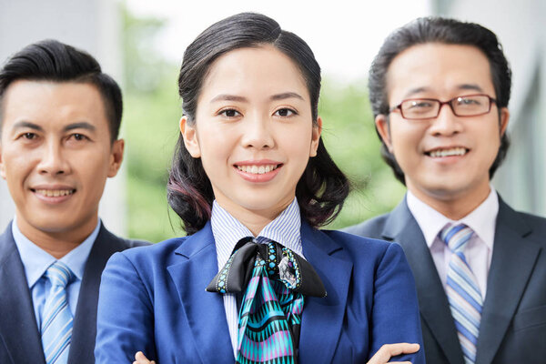 Elegant young Asian woman and men in suits smiling together at camera standing outdoors