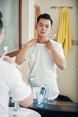 Diş fırçası tutan ve kendisi de banyo ayna yansıması arıyorum genç modern Asya adam