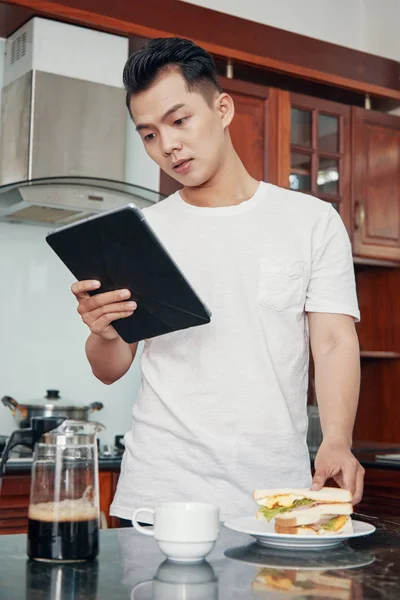 Casual Asiatico Uomo Guardando Tablet Cucina Mentre Mangiare Panino Con — Foto Stock