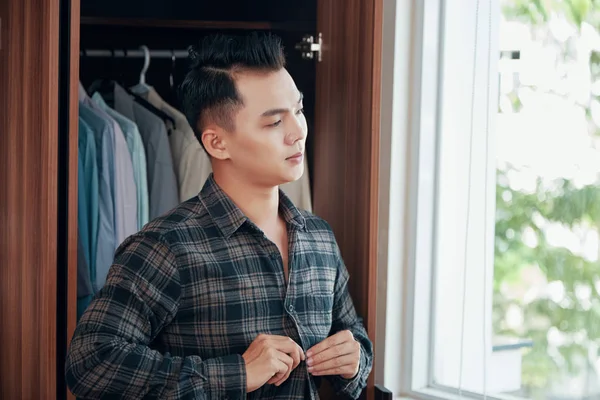 Hombre Asiático Abotonando Camisa Cuadros Mientras Viste Habitación Con Armario —  Fotos de Stock