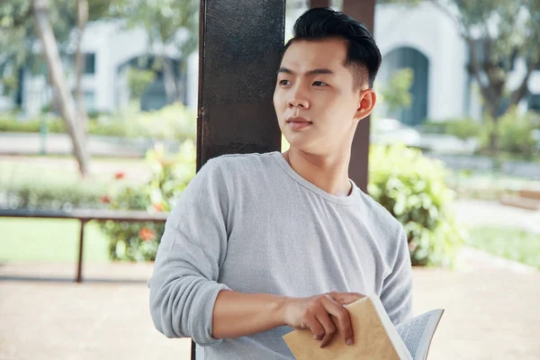 Atraktivní Asijské Chlap Drží Knihu Hledat Dál Zatímco Sedí Rozostřeného — Stock fotografie