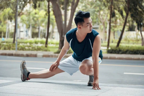 在阳光明媚的日子里 英俊的亚洲人在马路附近锻炼腿上的运动 把目光移开 — 图库照片