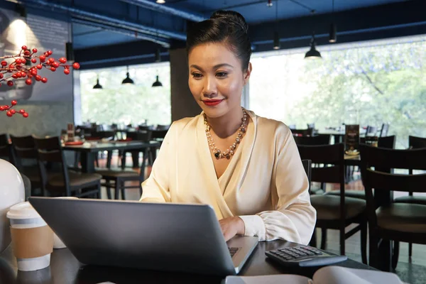 木製テーブルでレストランで座っていると 背景をぼかした写真のラップトップを使用して白いブラウスのアジア女性実業家幸せ — ストック写真