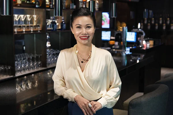 美丽的微笑迷人的年轻亚洲女人在优雅的衣服站在放松靠在黑暗闪亮的咖啡馆酒吧柜台 — 图库照片