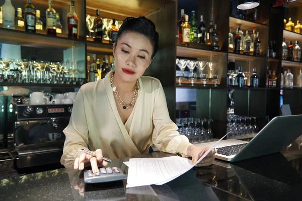 美丽的亚洲女酒保专注于使用计算器在酒吧做商业帐户 — 图库照片