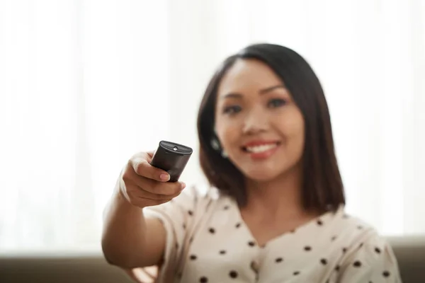 Smiling woman changing channels with remote control