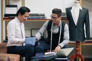 Neşeli terzi ve istemci için takım elbise kumaş tartışıyor 