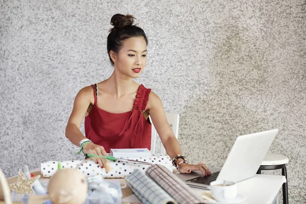 年轻的亚洲妇女坐在桌旁 在笔记本电脑上寻找关于如何用礼品纸包装礼物的大师班 — 图库照片