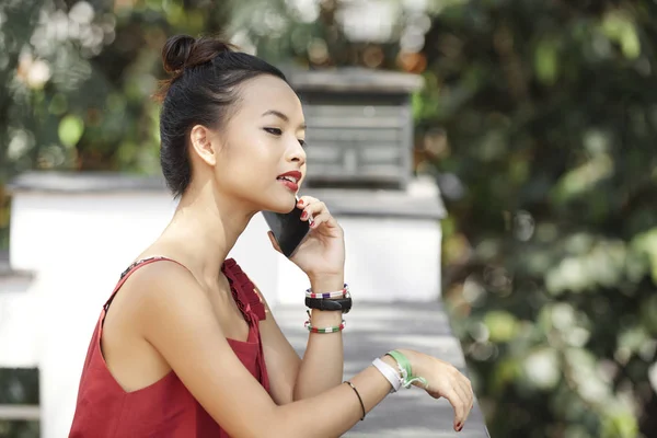 若いアジア女性彼女のスマート フォンを持って 屋外で立っている間電話で誰かに聞いて — ストック写真
