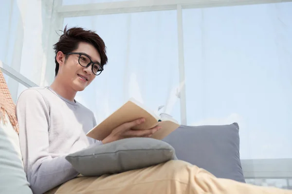 Όμορφος Ασίας Άντρας Κάθεται Στο Κρεβάτι Και Την Ανάγνωση Ενδιαφέρον — Φωτογραφία Αρχείου