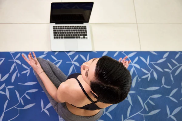 ノート パソコンの前でヨガマットのアジア若いブルネットの瞑想の高いビューのイメージ — ストック写真