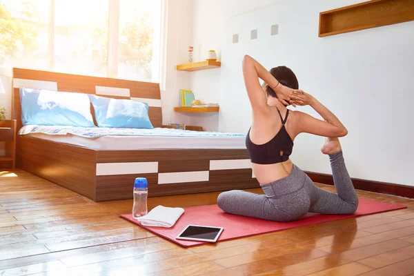 スポーツウェア運動マットの上に座って 彼女のベッドの寝室の前でストレッチ体操を行うの若い女の子の背面図 — ストック写真