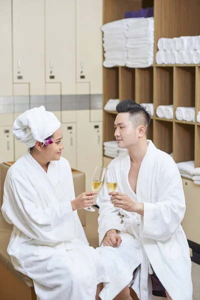 若いアジアのカップル バスローブで座っていると ウェルネス センターでドレッシング ルームでシャンパンのグラスで乾杯 — ストック写真