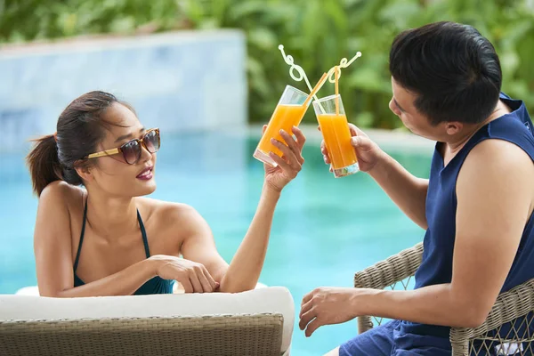 年轻的亚洲夫妇在户外游泳池附近晒太阳 并喝鸡尾酒敬酒 — 图库照片