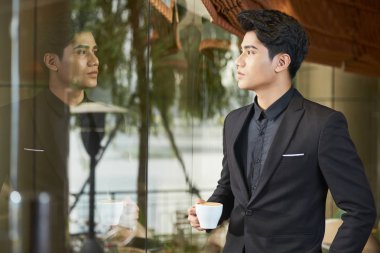Kendine güvenen genç Vietnamlı işadamı portresi pencereden bakarak kahve ile