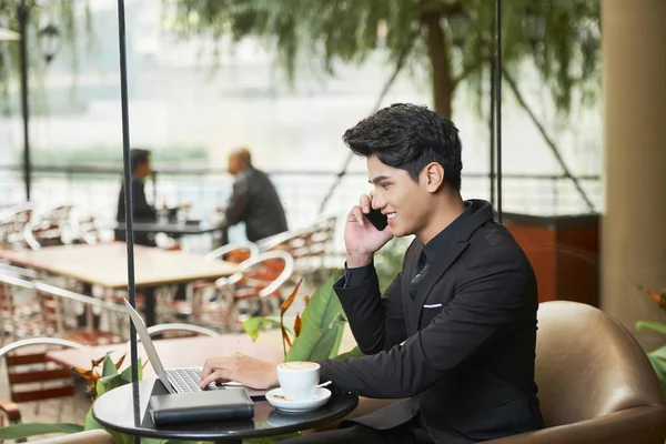 Красивый Улыбающийся Бизнесмен Разговаривающий Телефону Работающий Ноутбуке Сидя Столиком Кафе — стоковое фото