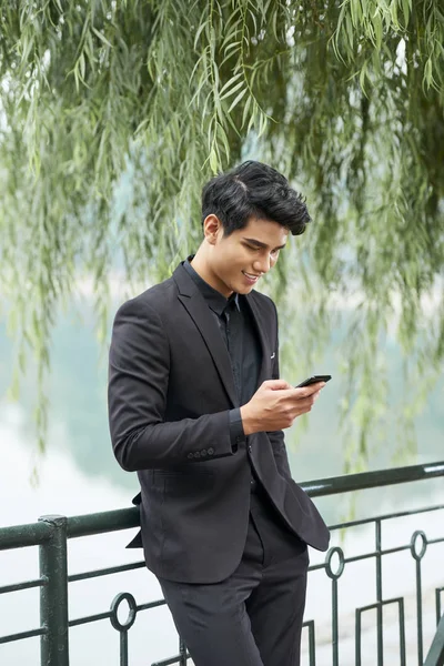 Sorrindo Jovem Bonito Asiático Homem Terno Encostado Cerca Parque Mensagens — Fotografia de Stock