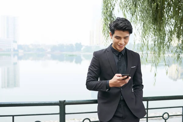 屋外に立っているとき 彼の携帯電話をチェック肯定的な若いベトナム人経営者の肖像 — ストック写真