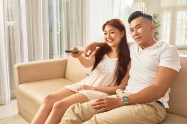 Kanepede oturan ve birlikte evde film izlerken sırasında gülümseyen genç Asyalı Çift