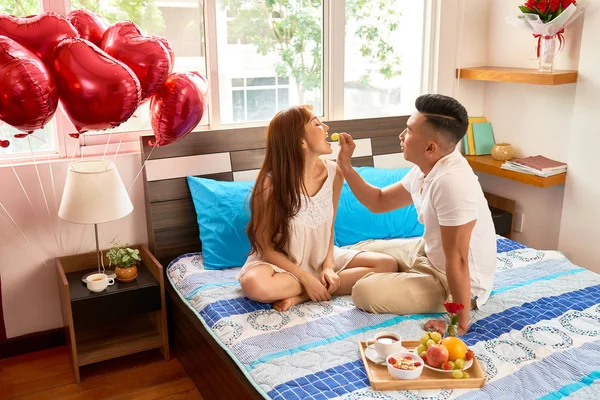 Jongeman Voeding Zijn Vriendin Met Druivenmost Terwijl Zij Zittend Bed — Stockfoto