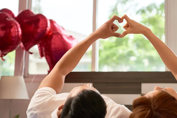 年轻的家庭一起躺在床上 用双手使自己的心形 他们在卧室里庆祝情人节 — 图库照片