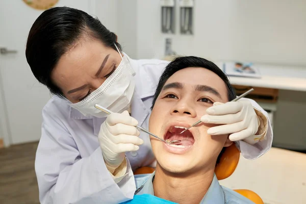 在医院坐在牙科椅上的亚洲男子戴口罩和制服检查牙齿健康的医生妇女 — 图库照片