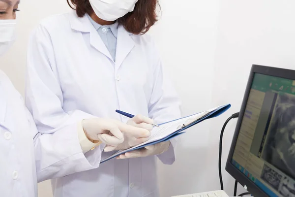 Crop shot of doctors examining panoramic x-ray on computer screen and assistant taking notes on clipboard