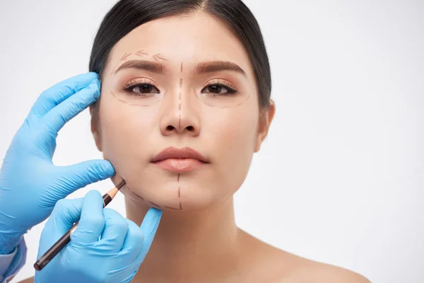 Cosmetic surgeon drawing lines on face of young beautiful woman