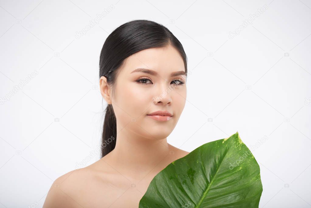 Beautiful young woman with flawless skin holding big green leaf