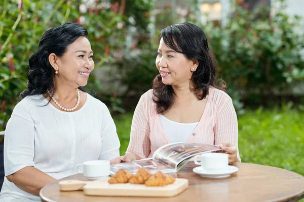迷人的时尚亚洲老年妇女聊天和微笑 而坐在户外的桌子与茶和羊角面包 — 图库照片